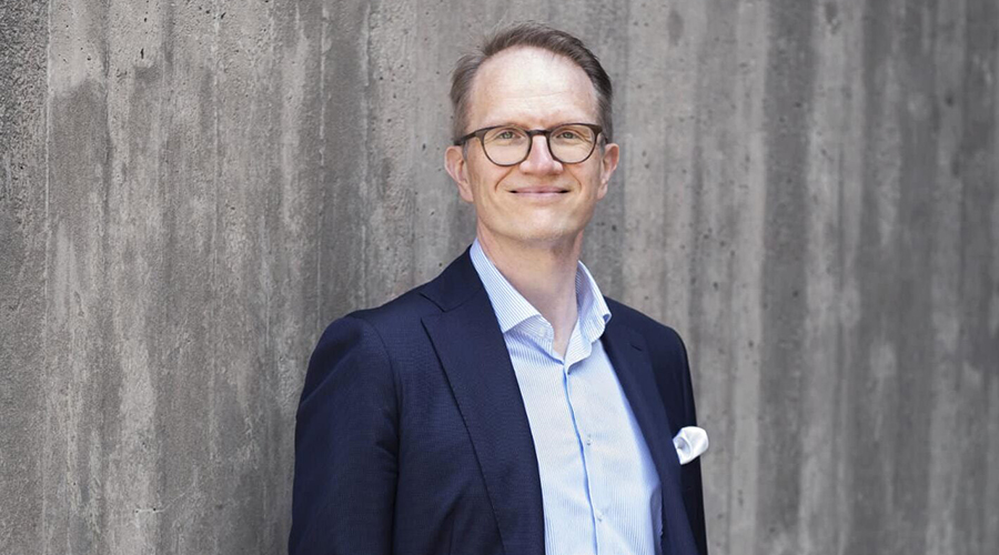 Timo Vesala harmaan betoniseinän edessä kuvattuna.